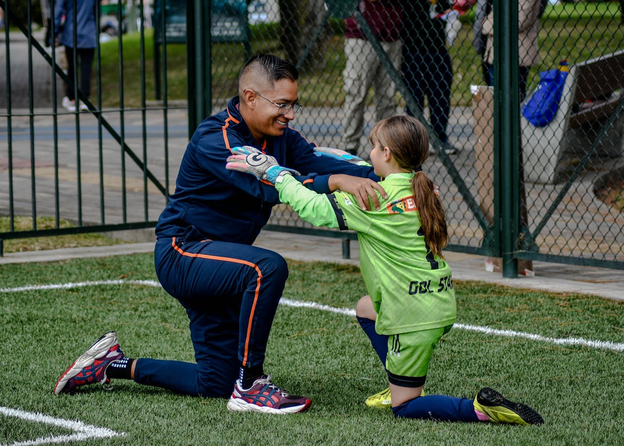 A coach kneels to encourage a young female soccer player in a game.